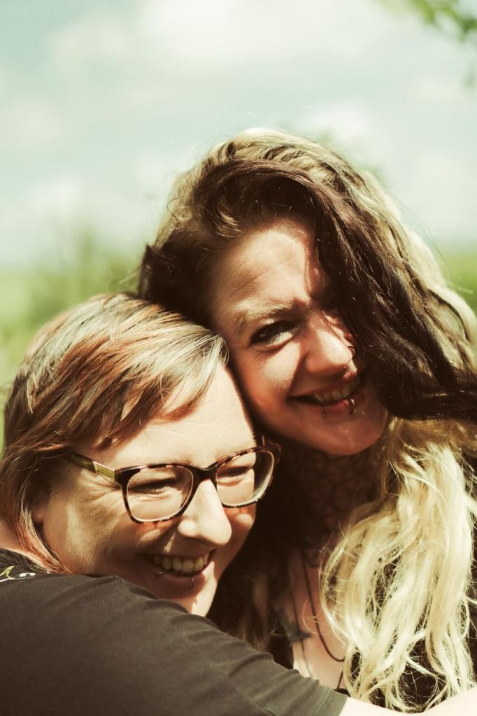 2 women embracing, and smiling.